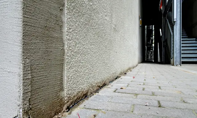 Die Ecke eines Gebäudes wird mit WDVS verputzt. Der Putz ist rau und hellgrau, mit sichtbaren Spuren der Verarbeitung.