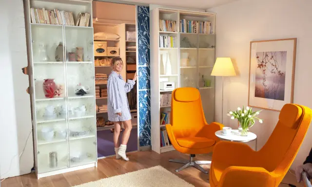 Frau steht vor einem begehbaren Kleiderschrank, den sie selber machen könnte. Links ein Regal mit Geschirr, rechts ein Regal mit Büchern.
