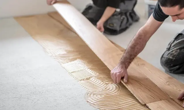 Handwerker verlegen sorgfältig Parkett. Kleber wird auf den Boden aufgetragen, bevor die Holzplanken präzise platziert werden.