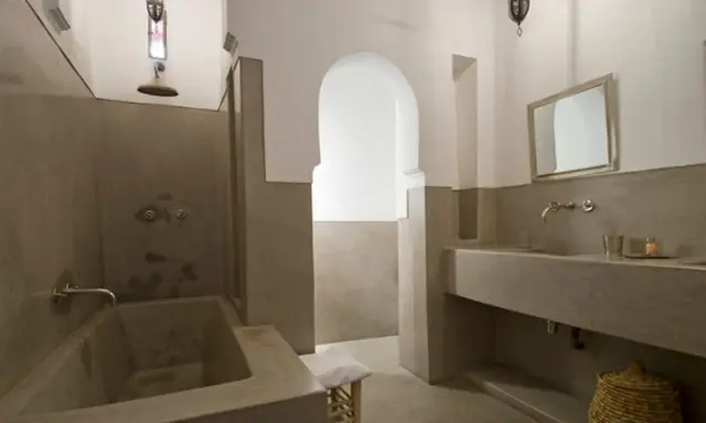 Modernes Badezimmer mit einer freistehenden Badewanne und einem Waschbecken aus Tadelakt. Ein großer Spiegel und ein traditioneller Korb vervollständigen den Look.