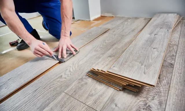 Handwerker misst Laminat für die Verlegung. Die Kosten für Laminat verlegen sind oft überschaubar.