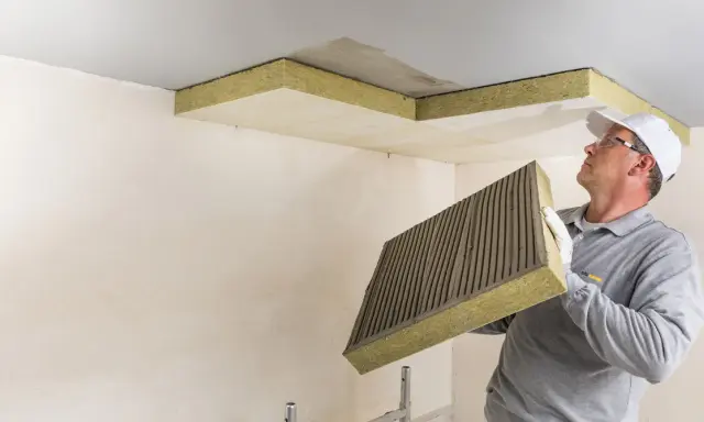 Mann mit Kleber auf Dämmplatte bereitet vor, die Decke zu isolieren.