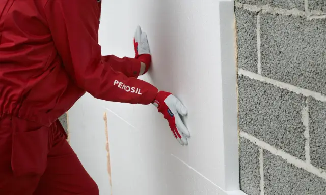 Hand mit Handschuh drückt WDVS Schaum an eine Betonwand.