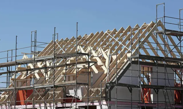 Holzkonstruktion eines Dachstuhls im Bau, umgeben von Gerüsten. Ein Architekt plant den Bau dieses Hauses.