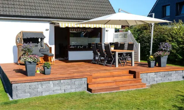 Eine schöne garten terrasse mit Holzdielen, Sitzmöbeln, Sonnenschirm und Blumen. Perfekt für entspannte Stunden im Freien.