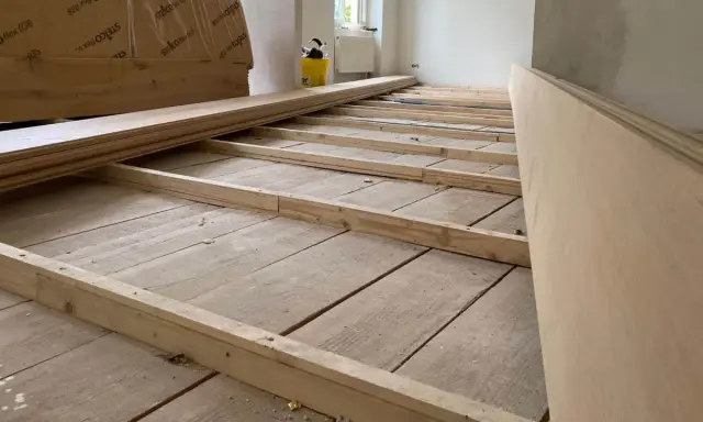 Holzbalken werden auf alten Dielen verlegt, um den Untergrund für einen neuen Dielenboden auszugleichen.