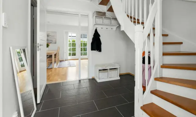 Helle Diele mit dunklem Fliesenboden, Spiegel, Garderobe und einer weißen Treppe, die auf eine **steintreppe renovieren**-Idee hindeutet.