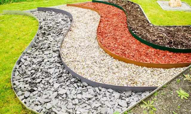 Geschwungene Beete mit verschiedenen Schichten aus grauem Schiefer, hellem Kies, roter Rindenmulch und dunklem Rindenmulch, die durch Metallkanten für rasenkanten setzen getrennt sind.