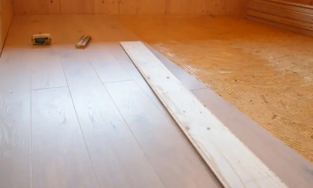 Holzboden wird verlegt. OSB-Platten sind mit Kleber vorbereitet, darauf werden helle Dielen verlegt.