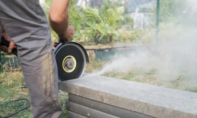 Mann schneidet mit Winkelschleifer Terrassenplatten. Staub wirbelt auf.