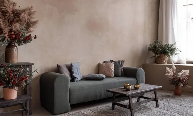 Gemütliches Wohnzimmer mit Sofa, Holztisch und rustikalen Dekorationen vor einer Wand mit **lime wash**-Oberfläche.