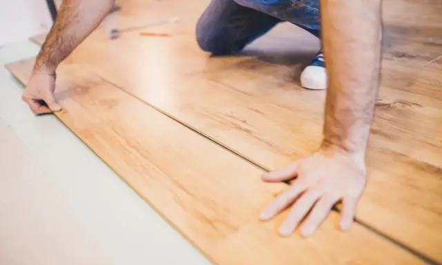 Mann verlegt Laminat. Die Holzoptik der Dielen wird sorgfältig zusammengefügt.