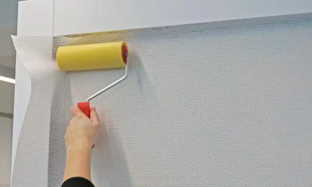 Mit einem gelben Farbroller wird eine weiße Tapete spachteln.