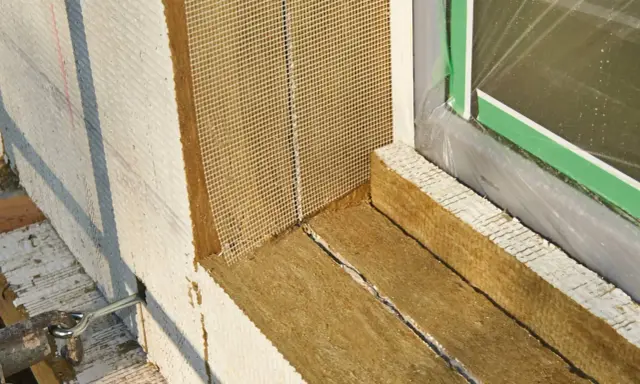 Fensterlaibung wird mit Steinwolle gedämmt. Das Material wird sorgfältig zugeschnitten und mit Armierungsgewebe versehen, um es vor dem Kleben vorzubereiten.