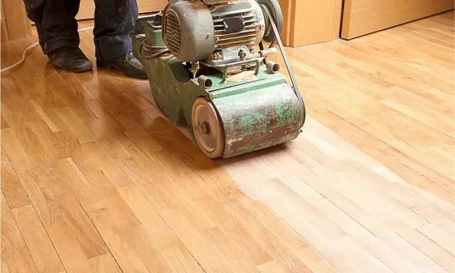 Ein Handwerker bearbeitet mit einer Schleifmaschine einen Holzboden. Das Parkett wird abgeschliffen, um ihm neues Leben einzuhauchen.