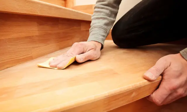 Mann schleift mit Sandpapier eine Holztreppe, um sie zu renovieren.