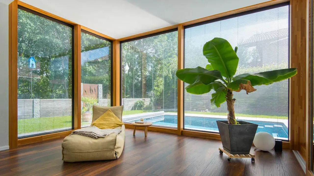 Gemütlicher Raum mit großem Fenster, Blick auf Pool & Garten. Informieren Sie sich über die Wintergarten Kosten für Ihr eigenes Paradies.