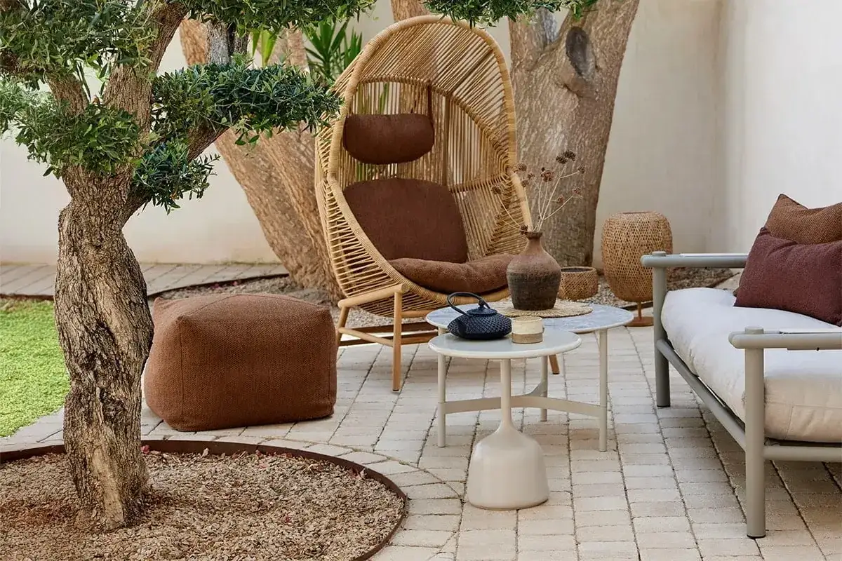 Gem&uuml;tliche kleine Terrasse gestalten mit Rattan-Sessel, Beistelltischen, Sofa und Pouf. Nat&uuml;rliche Materialien und erdige T&ouml;ne schaffen eine Oase.
