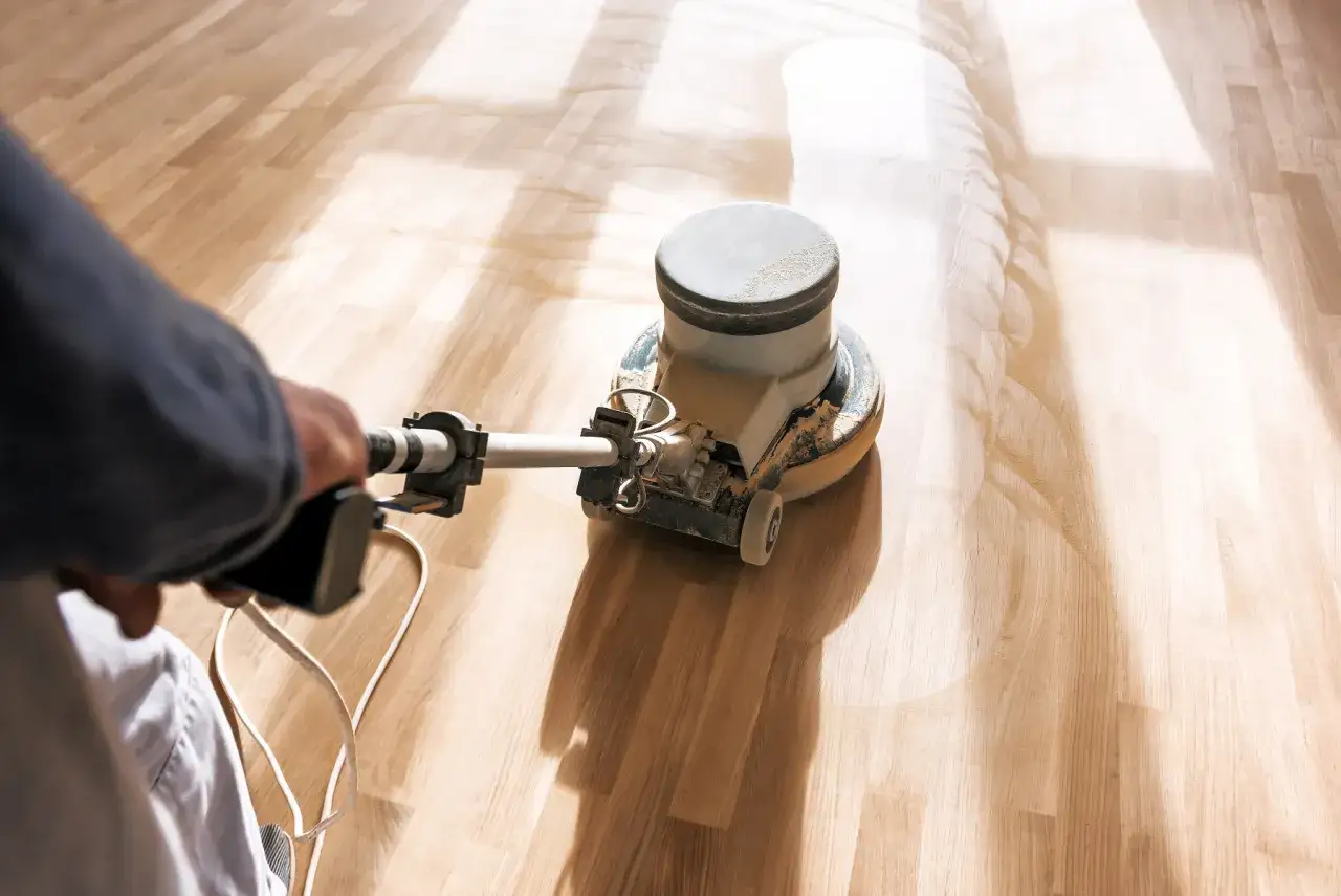 Ein Handwerker bearbeitet mit einer Maschine einen Holzboden. Das Parkett abschleifen l&auml;sst den Boden wieder wie neu aussehen.