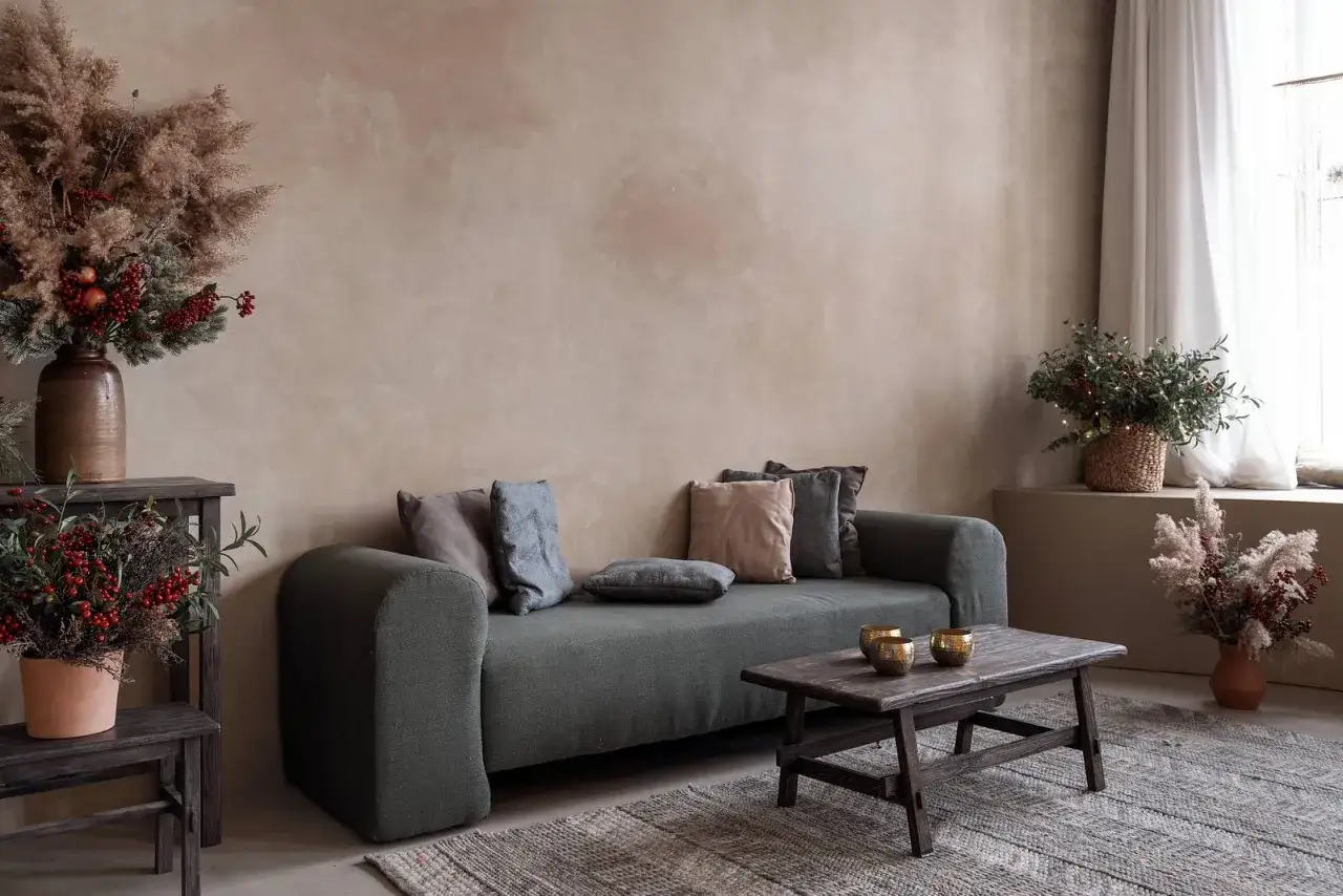 Gemütliches Wohnzimmer mit Sofa, Holztisch und rustikalen Dekorationen. Die Wand ist mit einer natürlichen lime wash Technik gestaltet.