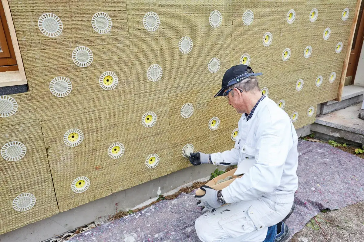Handwerker bringt befestigung in mineralwolle an. Die Fassade wird mit D&auml;mmplatten isoliert, die mit runden Elementen versehen sind.