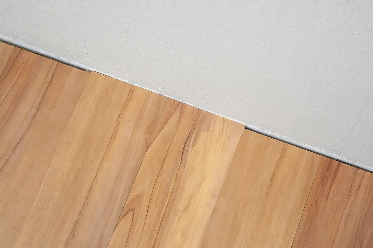 Nahaufnahme von Holzimitat-Laminat, das an einer Wand verlegt ist. Ein kleiner Spalt zeigt einen Fehler beim Laminat verlegen.