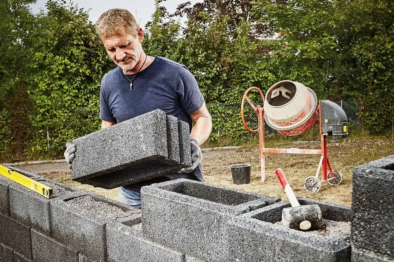 Mann legt Betonsteine für eine Mauer. Beton mischen ist der nächste Schritt.