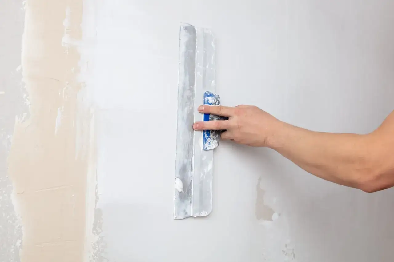 Hand spachtelt eine Wand. Die alte Tapete wird entfernt und die Wand f&uuml;r neue Tapete vorbereitet.