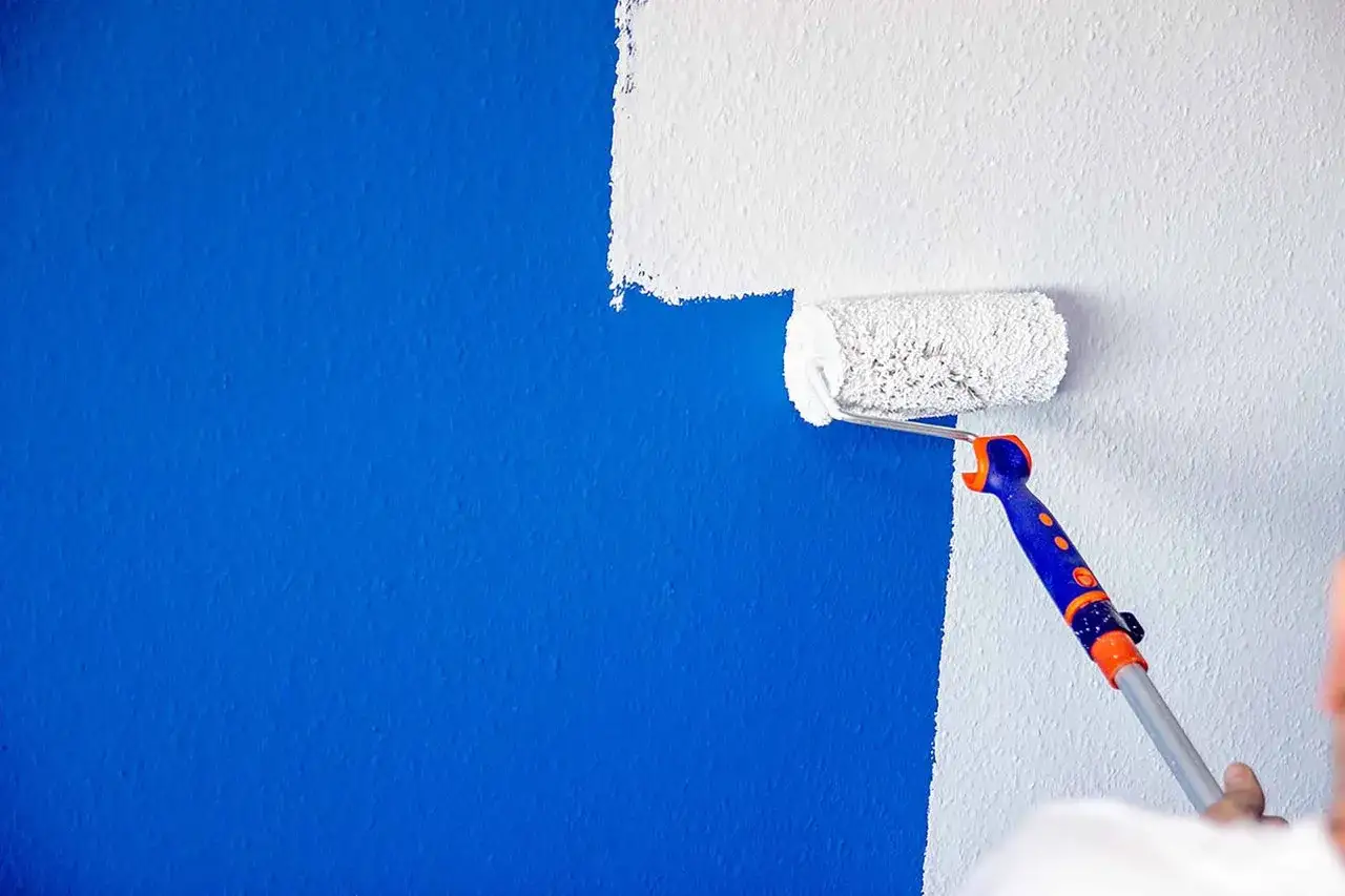 Eine blaue Wand wird mit weißer Farbe übermalt. Die weiße Farbe deckt gut und verwandelt die Wand.