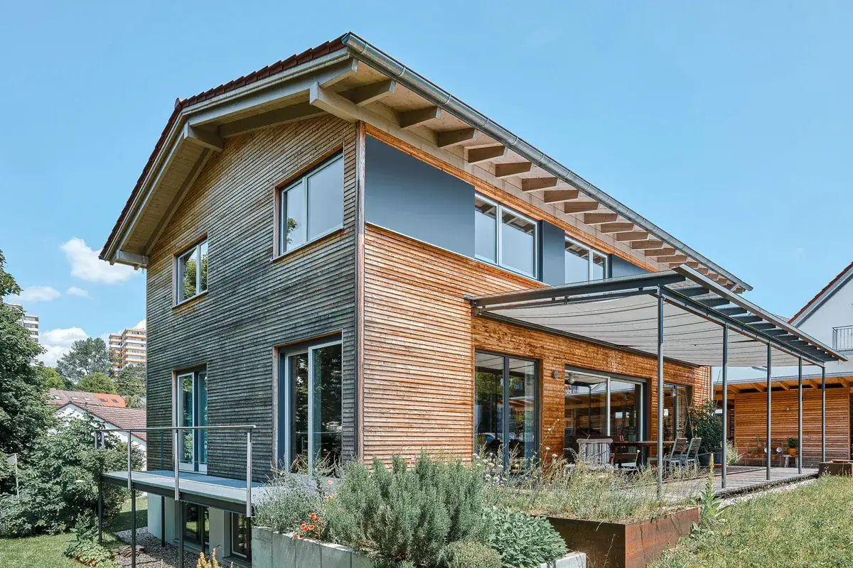 Modernes Holzhaus mit sichtbaren Dachsparren, das den klassischen Satteldach-Stil neu interpretiert. Gro&szlig;e Fensterfronten und eine Terrasse laden zum Verweilen ein.