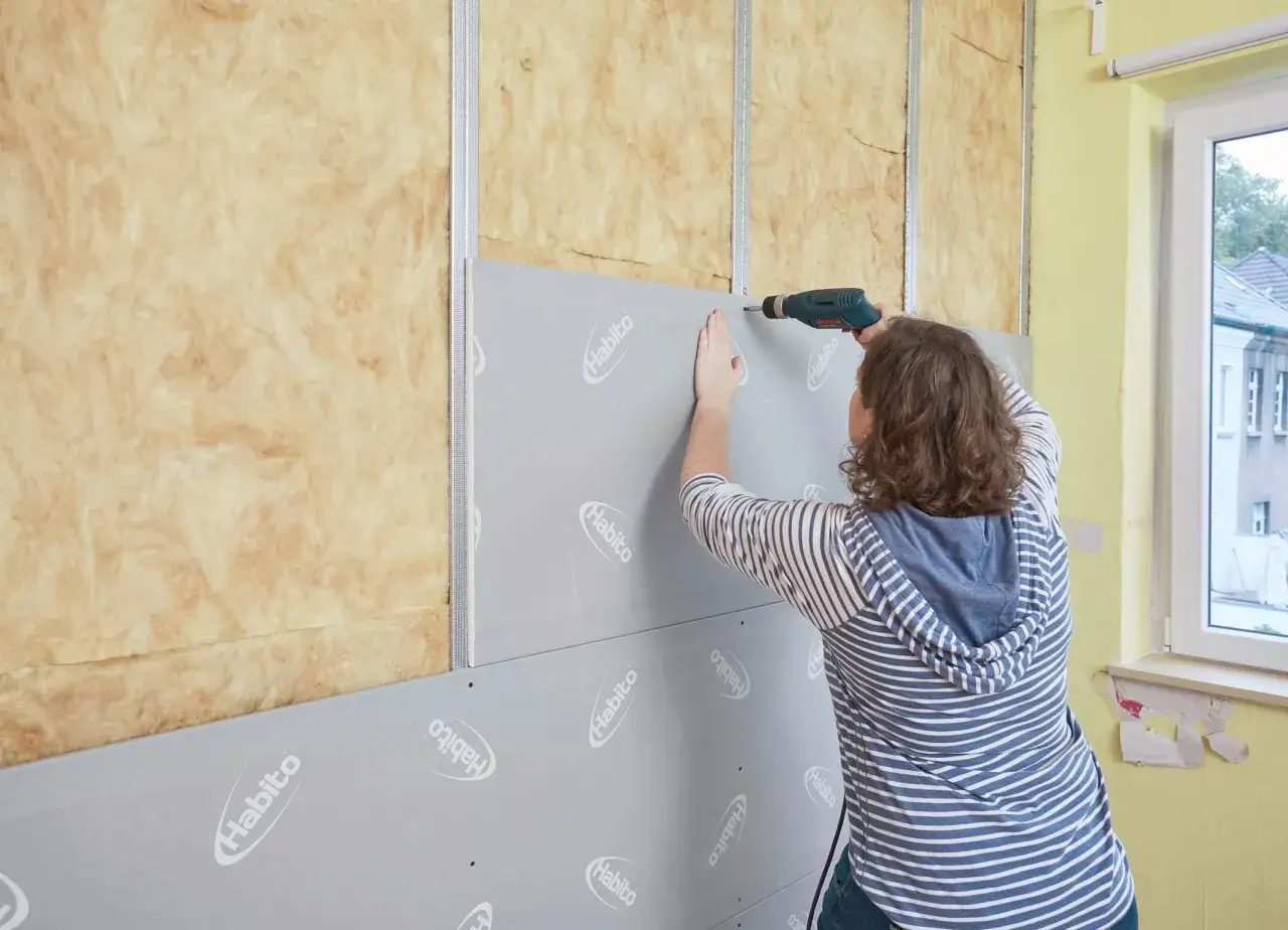 Frau schraubt Rigipsplatten an eine Wand mit D&auml;mmung. Die Platten werden mit einem Akkuschrauber befestigt.