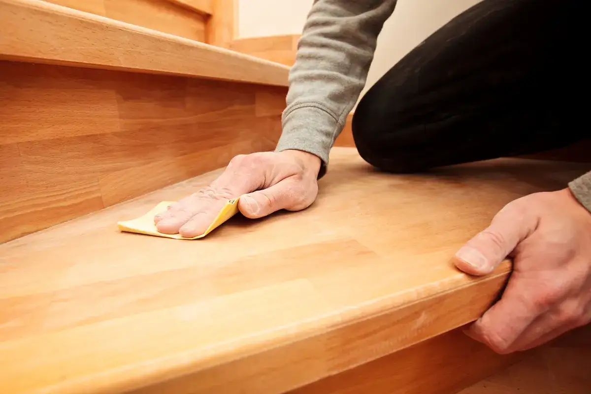 Mann schleift eine Holztreppe mit Schleifpapier. Die Renovierung der Holztreppe nimmt Gestalt an.