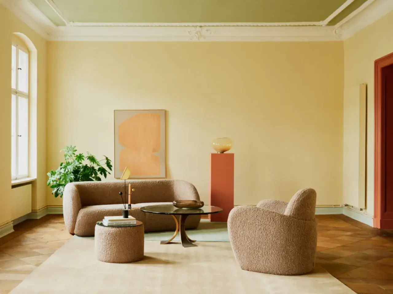 Ein Wohnzimmer mit gelben W&auml;nden und einer gr&uuml;nen Decke, die frisch gestrichen wurde. Ein beiger Teppich liegt auf dem Parkettboden.