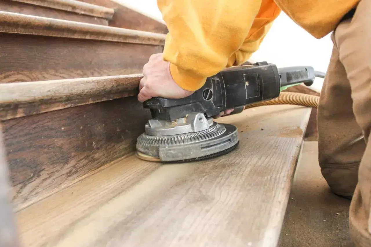 Hand schleift mit einer Maschine die Holztreppe, um den Boden für eine neue Behandlung vorzubereiten.