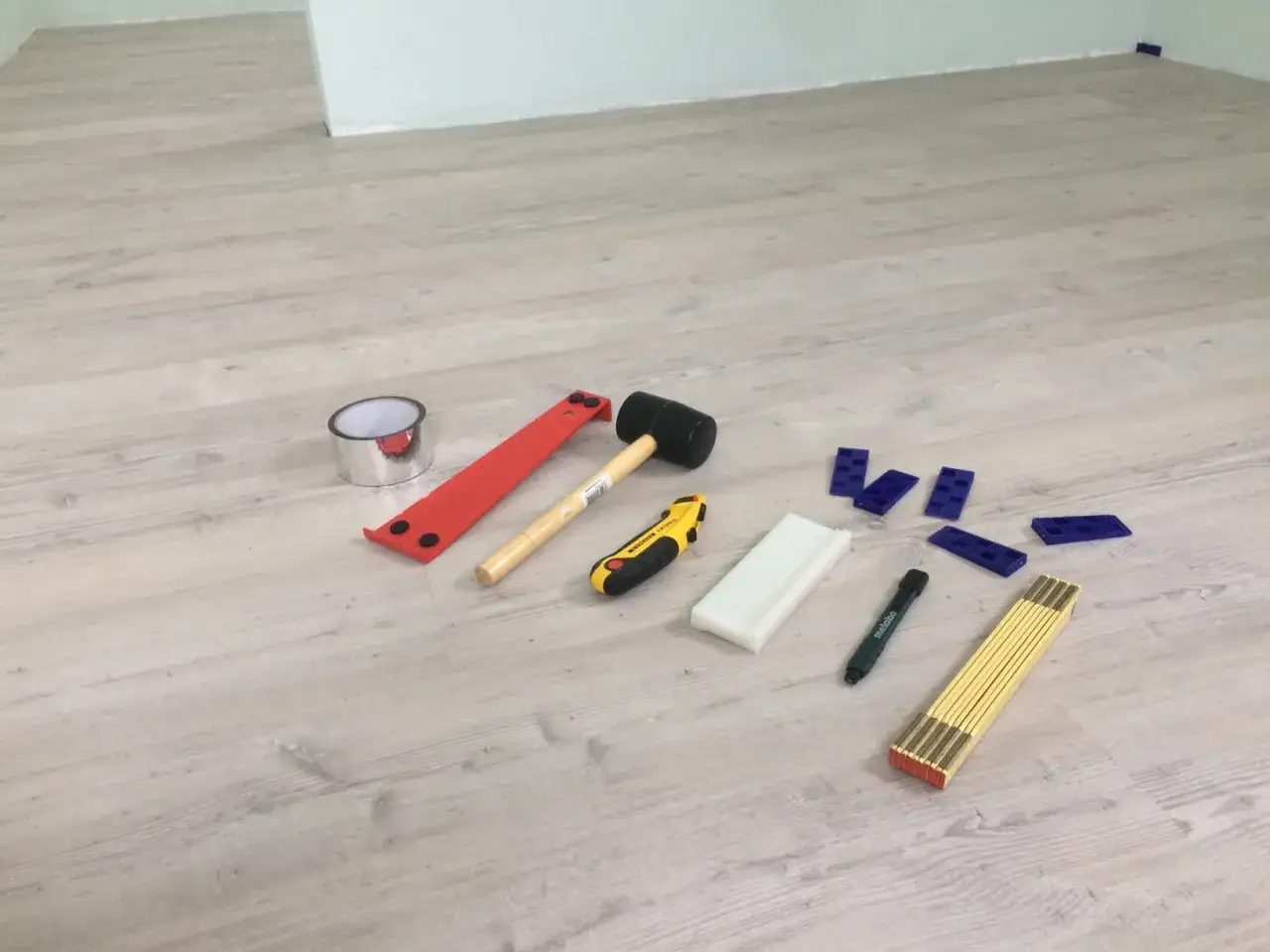 Werkzeuge für das Boden legen: Gummihammer, Cuttermesser, Distanzkeile, Maßband und mehr liegen bereit.