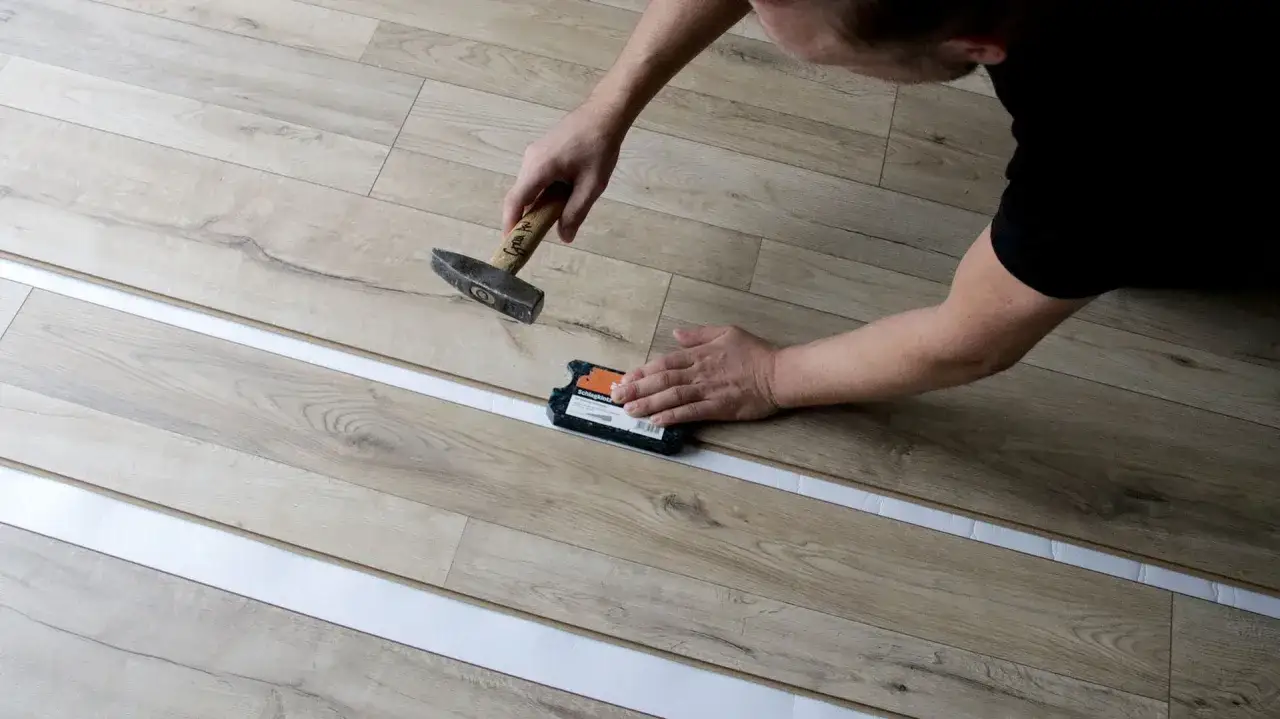 Mann verlegt Laminat und nutzt einen Schlagklotz, um die laminat dehnungsfuge korrekt zu setzen.