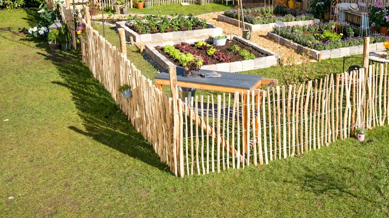 Ein rustikaler Holzzaun setzen um einen gepflegten Gem&uuml;segarten mit Hochbeeten und einer Sitzgelegenheit.