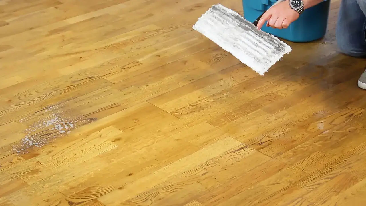 Ein Mann reinigt einen Holzboden mit einem Mopp. Die Parkett Pflege wird mit einem Reinigungsmittel durchgef&uuml;hrt, das Schaum hinterl&auml;sst.