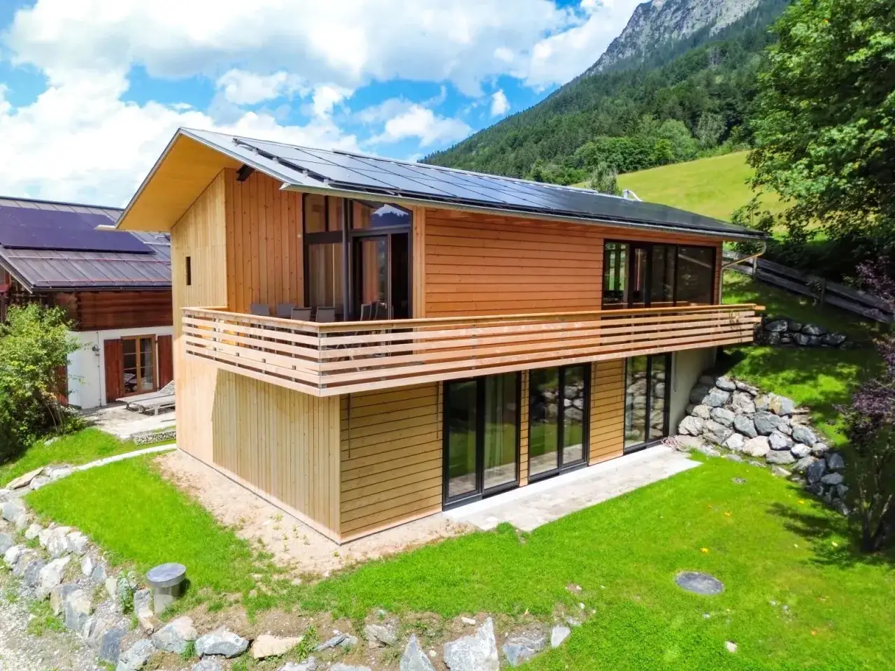 Modernes Holzhaus mit Solaranlage, Balkon und gro&szlig;en Fenstern. Ein Beispiel, was ein Chalet in den Bergen sein kann.