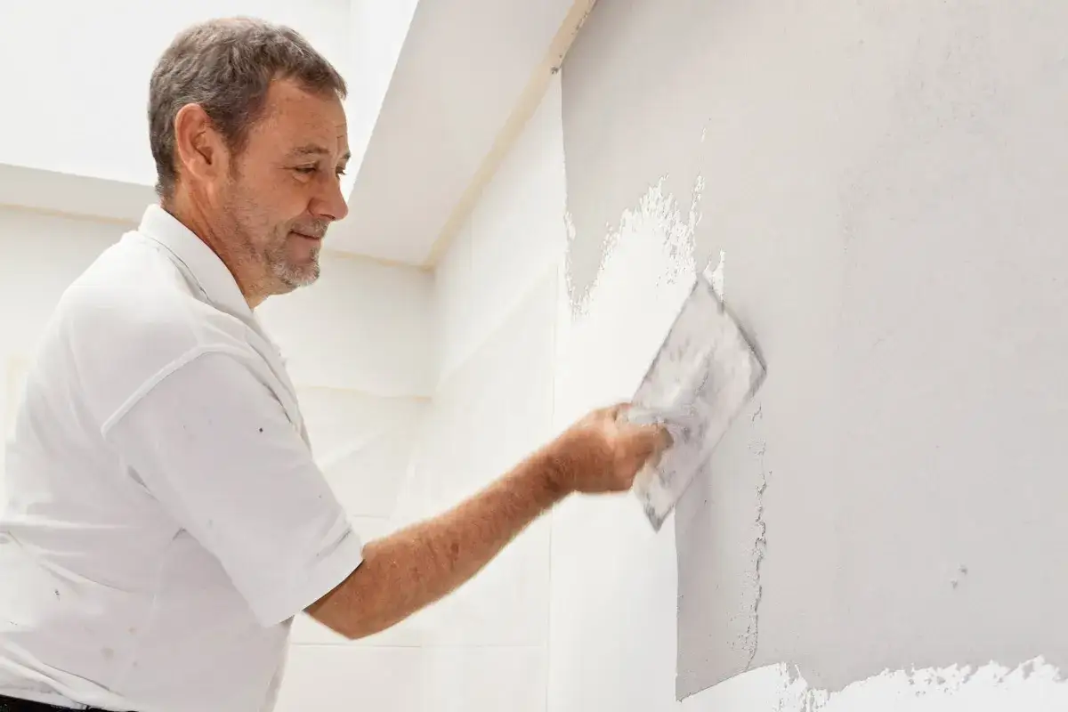 Mann verputzt eine Wand mit einer Kelle. Die Arbeit im Bad ist fast fertig.