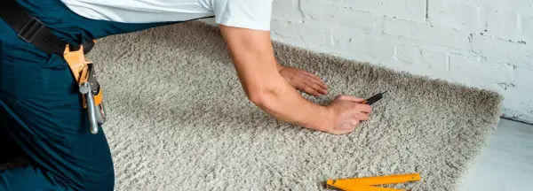 Handwerker verlegt Teppich mit einem Cuttermesser und einem Zollstock.