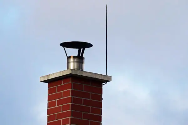 Ein roter Ziegelkamin mit einem Blitzableiter, der über dem Schornstein auf einem Haus thront, schützt vor Gewittern.