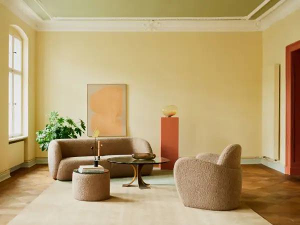 Ein Wohnzimmer mit gelben Wänden und einem frisch gestrichenen, hellgrünen Decke. Gemütliche Bouclé-Möbel und ein moderner Couchtisch laden zum Verweilen ein.