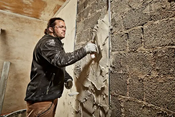 Mann verputzt eine grobe Ziegelwand mit einer Kelle. Der Putz wird gleichmäßig aufgetragen, um die Oberfläche zu glätten.