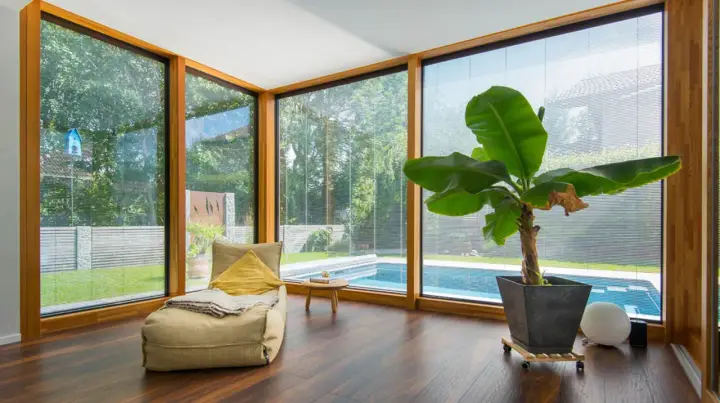 Gemütlicher Raum mit großem Fenster, Blick auf Pool & Garten. Informieren Sie sich über die Wintergarten Kosten für Ihr eigenes Paradies.